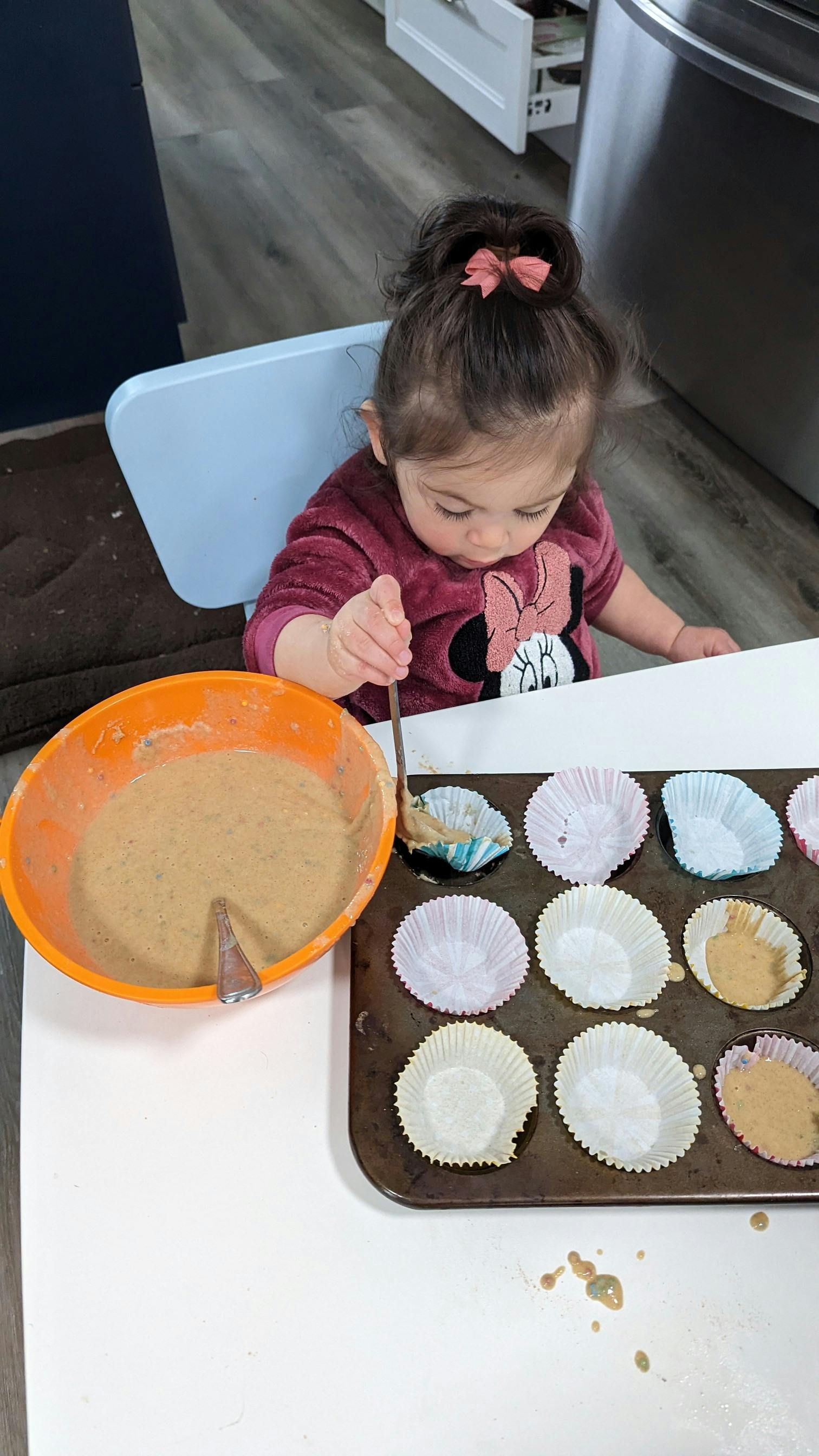 Child spooning batter from a bowl into a muffin tin