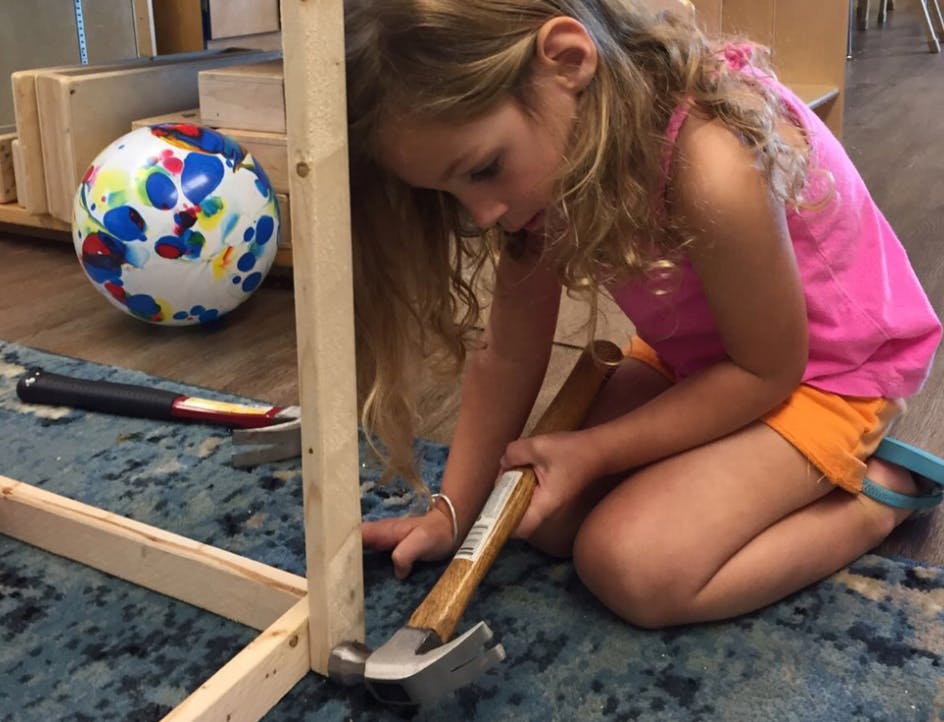 Child kneeling and hammering a wooden frame