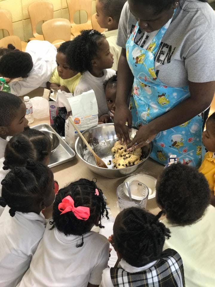 Person in apron mixing dough in a bowl with children watching