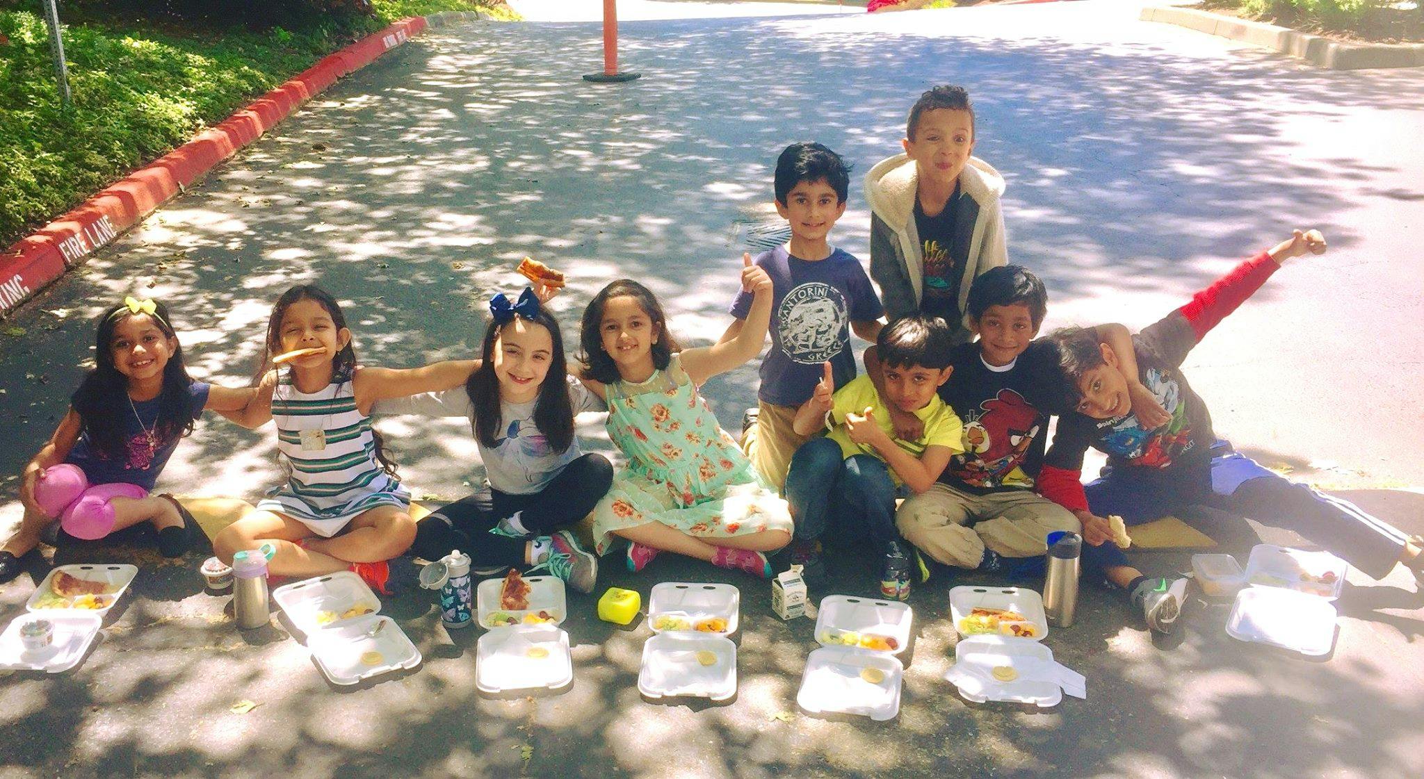 Group of children sitting on the ground with lunch containers