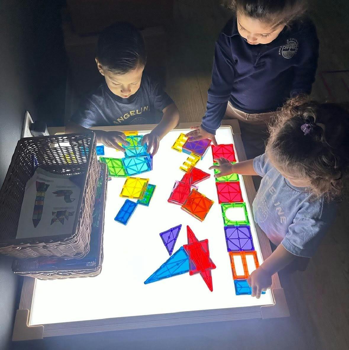Three children playing with translucent magnetic shapes on a light table