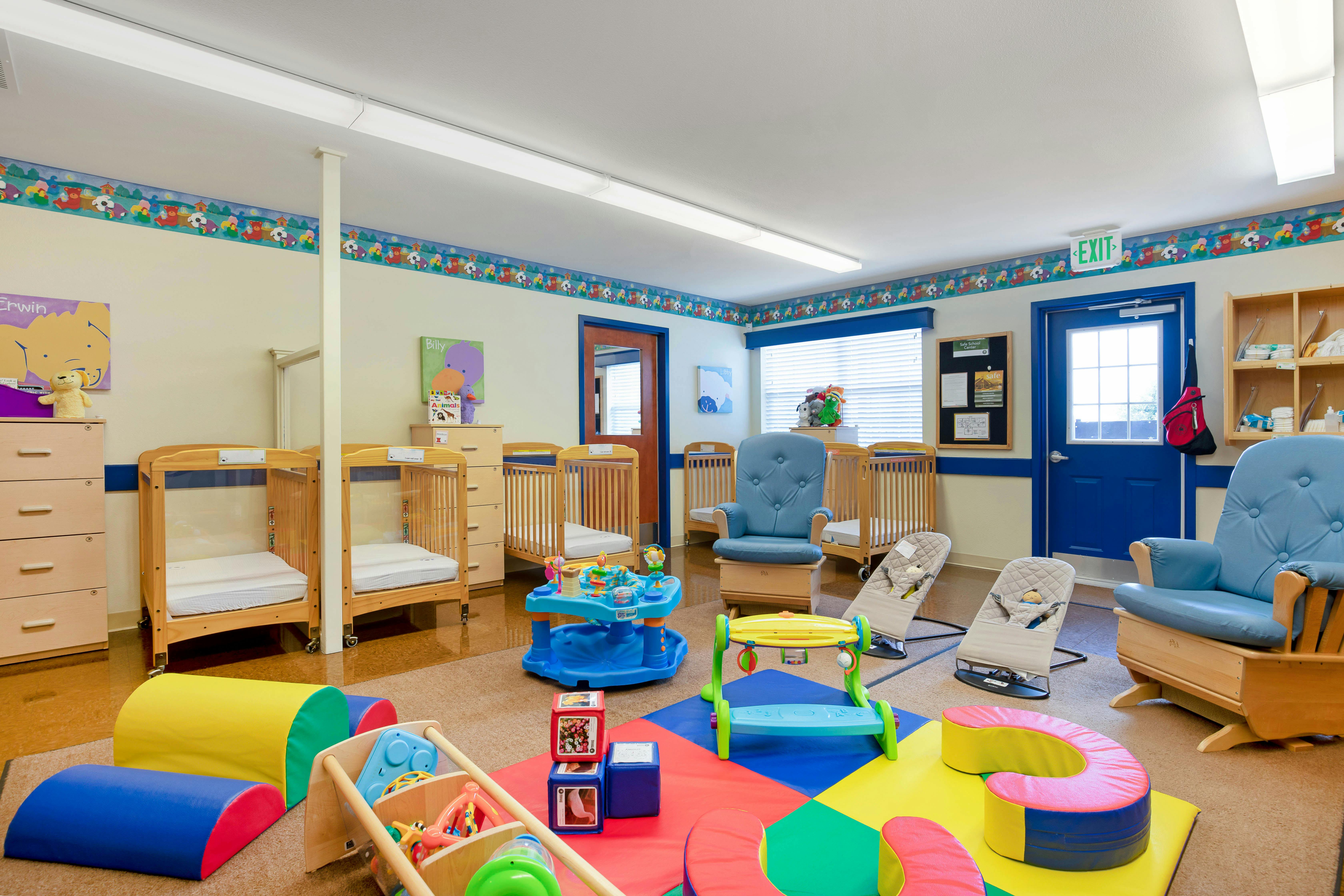A colorful baby nursery classroom with cribs, chairs, and play equipment