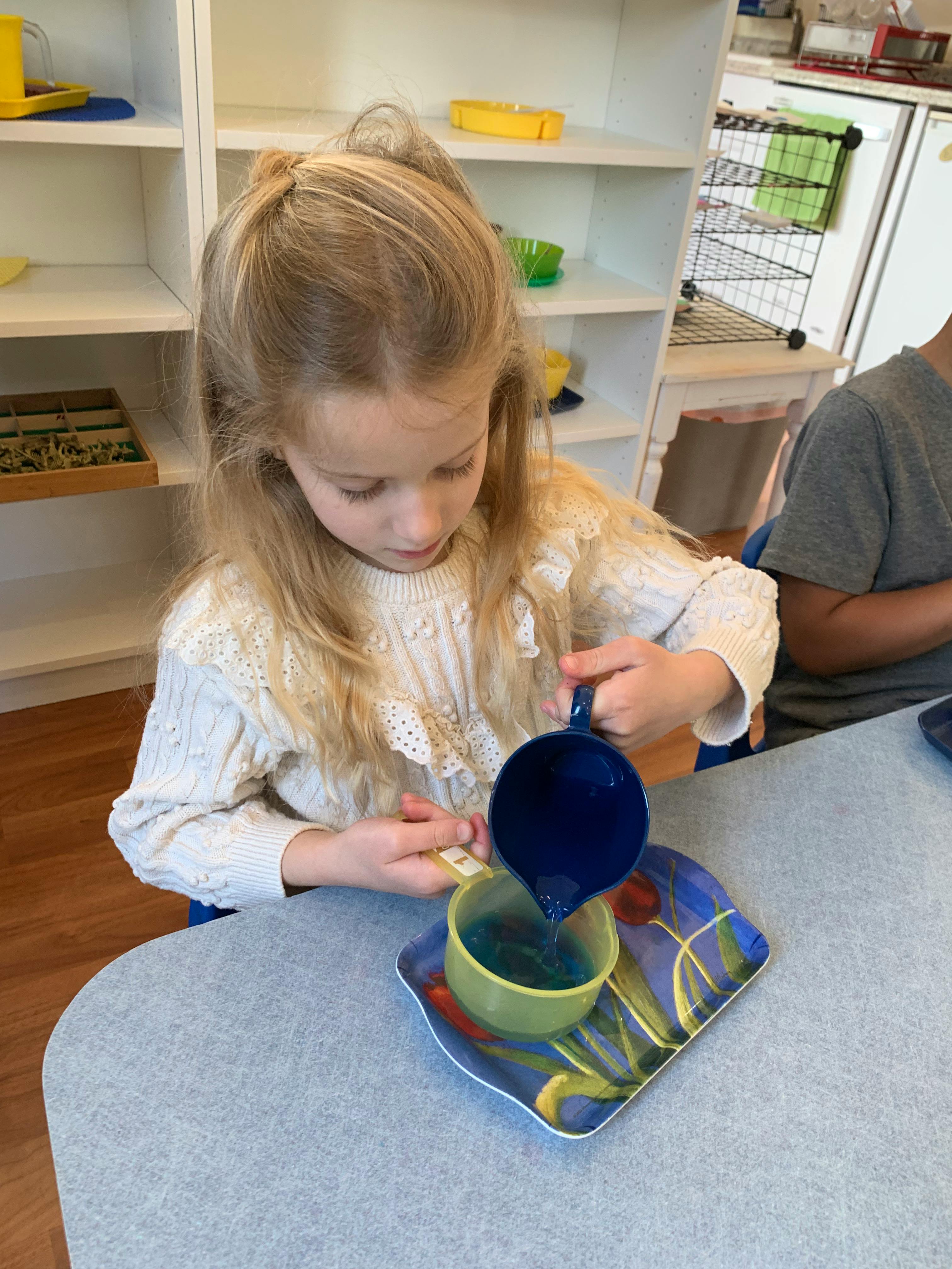 Child pouring liquid from a small pitcher into a cup
