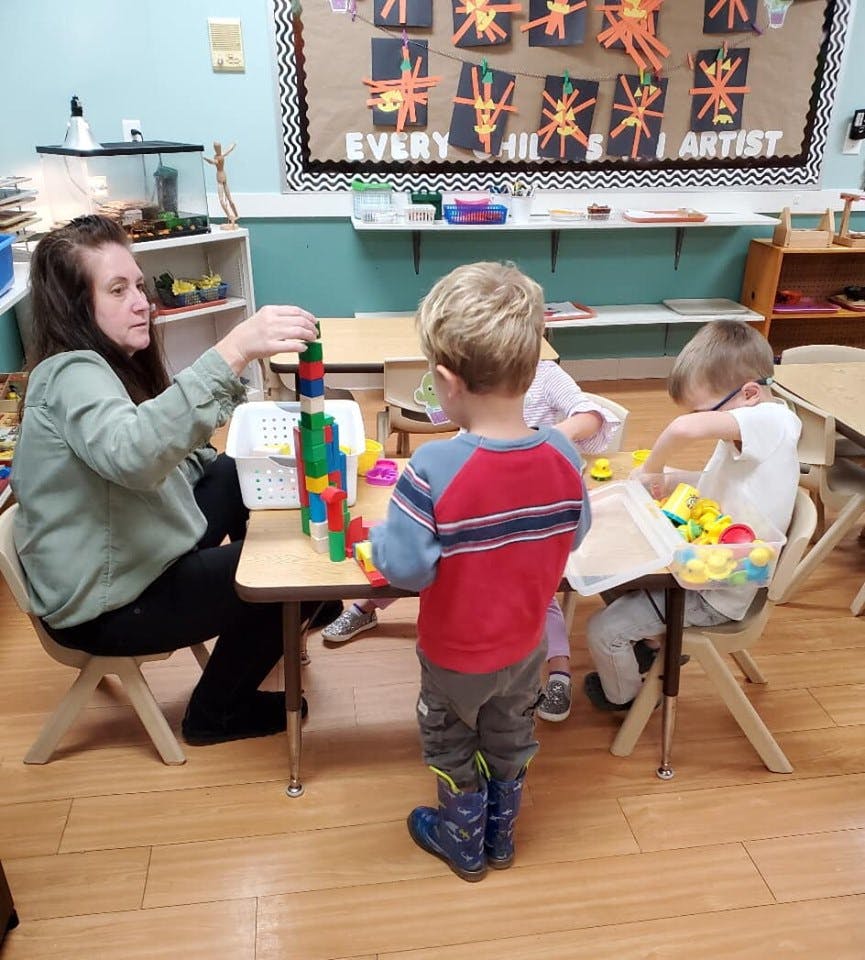 Adult and children playing with blocks at a table in a classroom