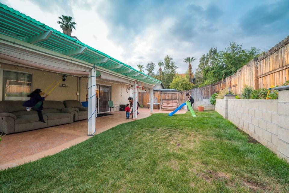 People on a patio and children playing in a backyard with a slide