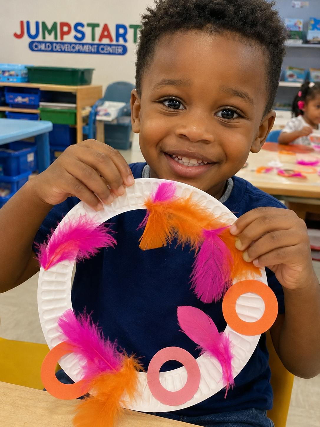 Smiling child holding up a paper plate craft decorated with feathers