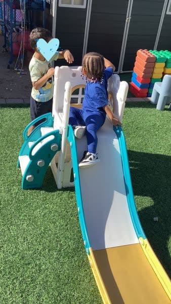 Two children playing on a slide and climbing structure outdoors