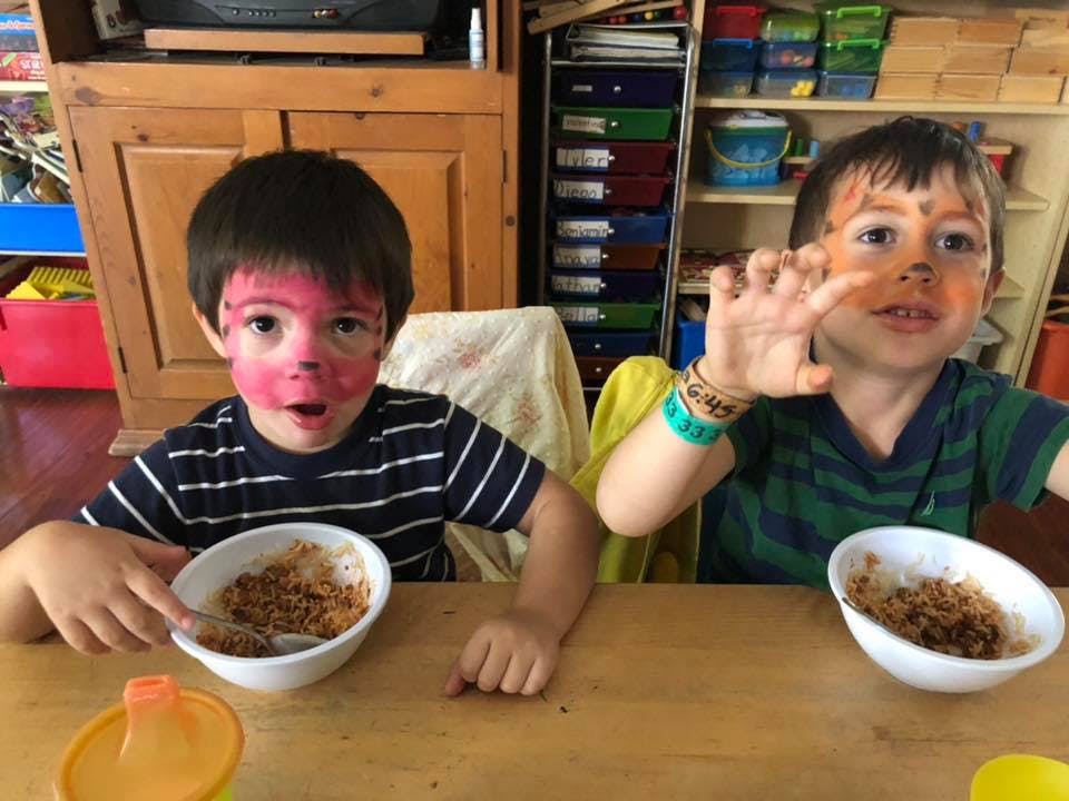 Two children with painted faces eating from bowls at a table