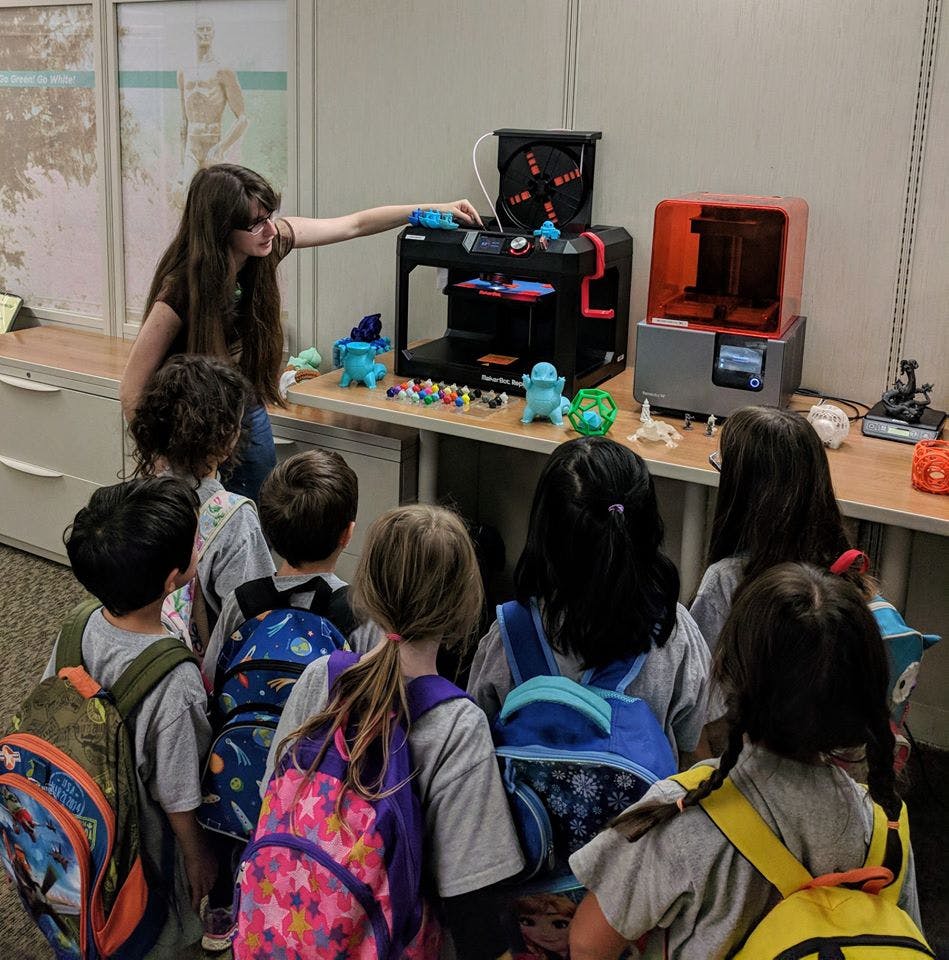 Person demonstrating a 3D printer to a group of children