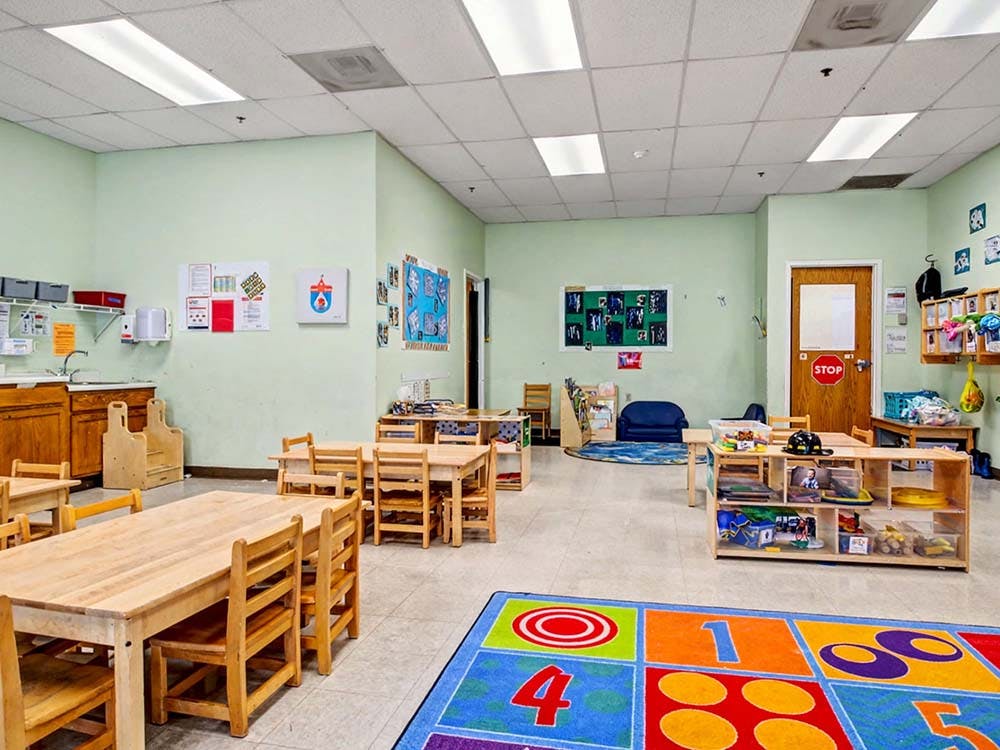 Empty classroom with small wooden tables and chairs, and a colorful rug
