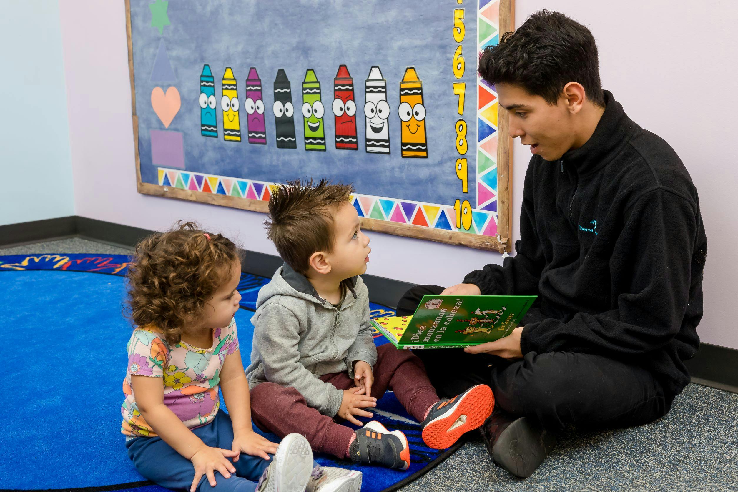 Person reading a book to two children in a classroom