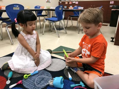 Two children playing with toys on a rug in a classroom