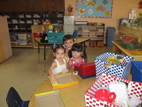 Three children at a table with boxes and baskets in a classroom