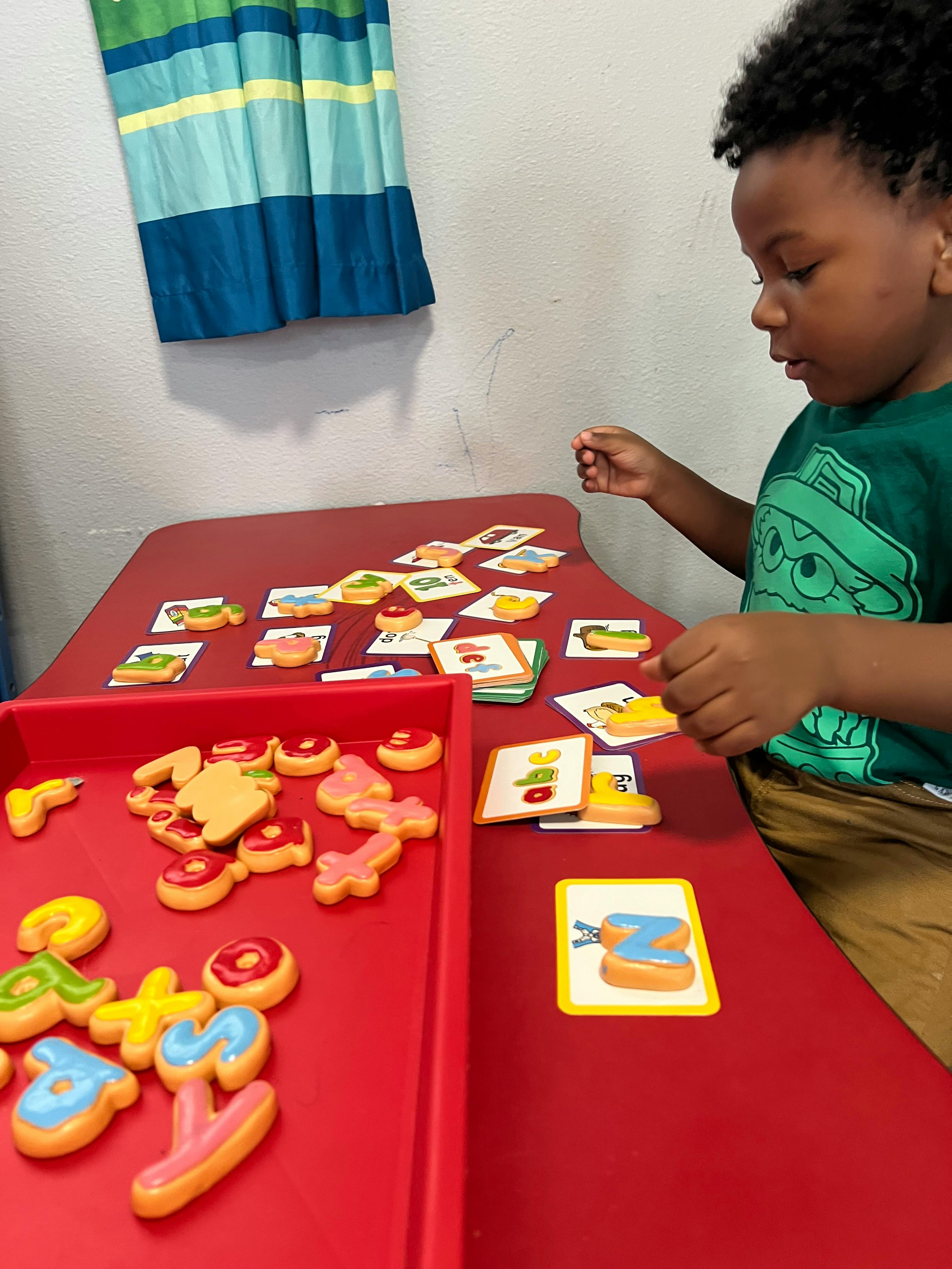 Child playing with alphabet letter toys and picture cards on a red table