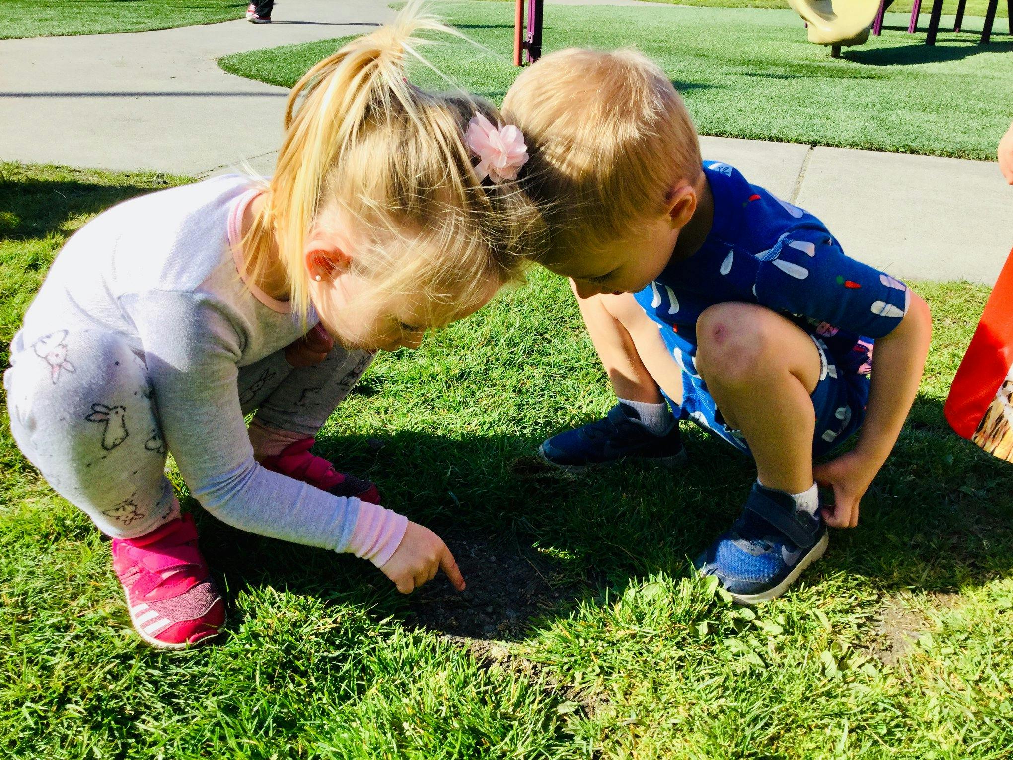 Two children crouching on grass, looking at something on the ground