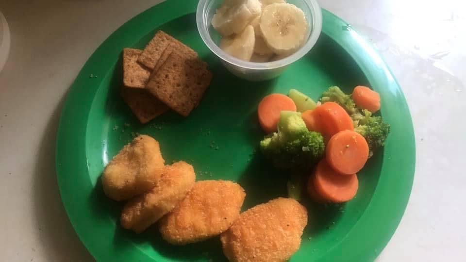 Chicken nuggets, crackers, bananas, and cooked carrots and broccoli on a plate