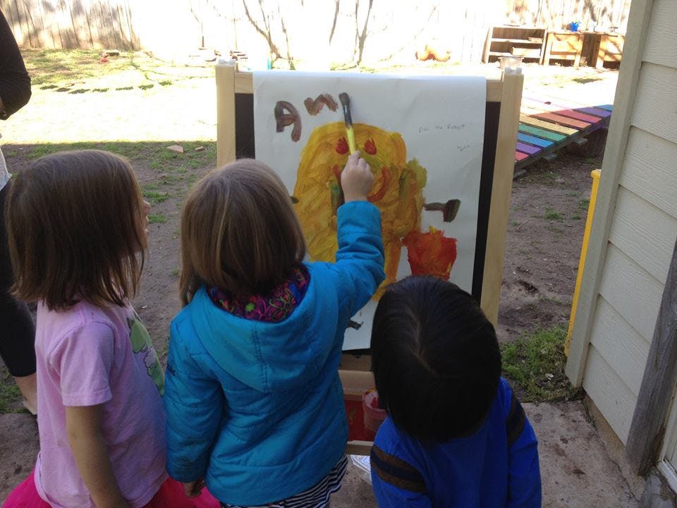 Three children painting on an easel outdoors