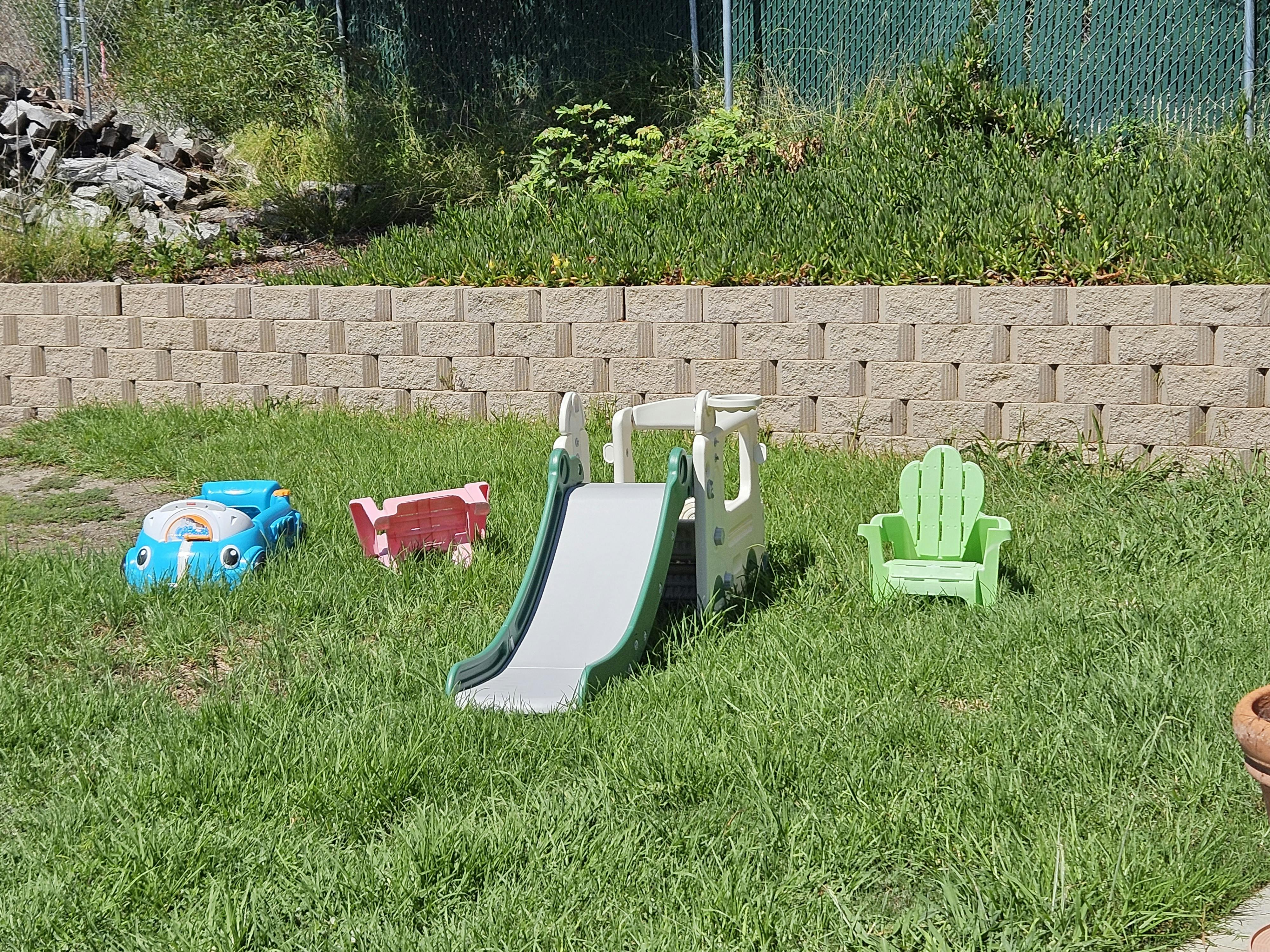 Children's slide, toy car, and chair in a grassy yard