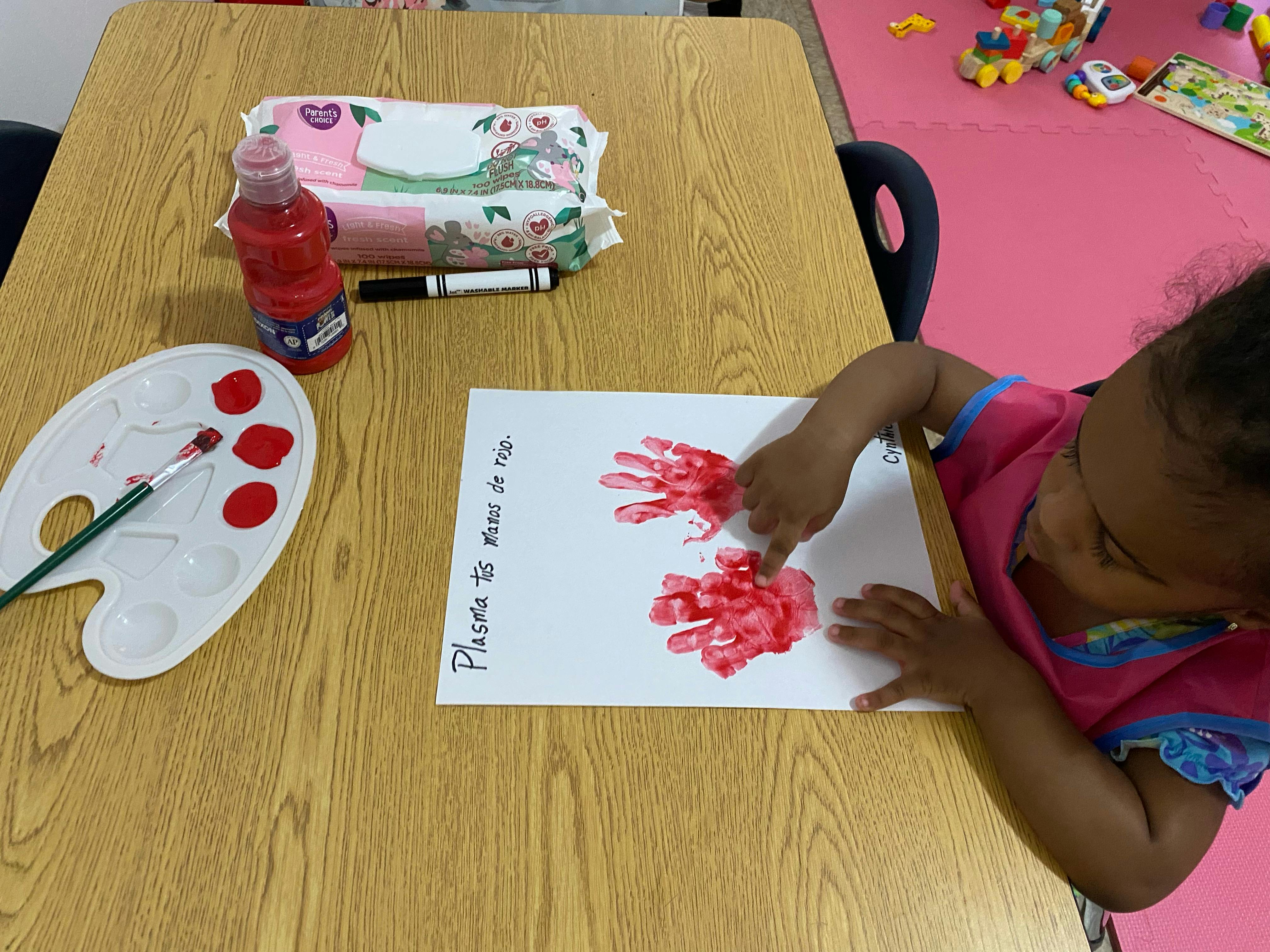 Child making red handprints on paper at a table