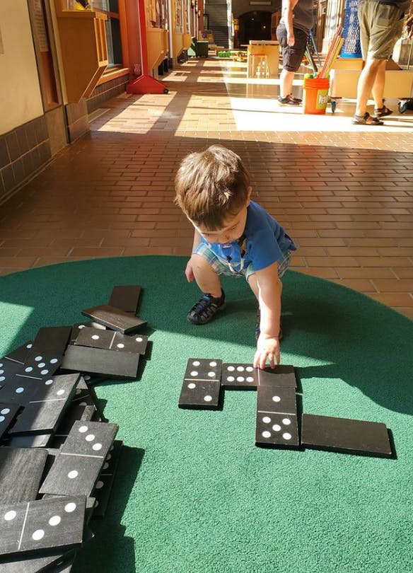 Child playing with large dominoes on a green surface
