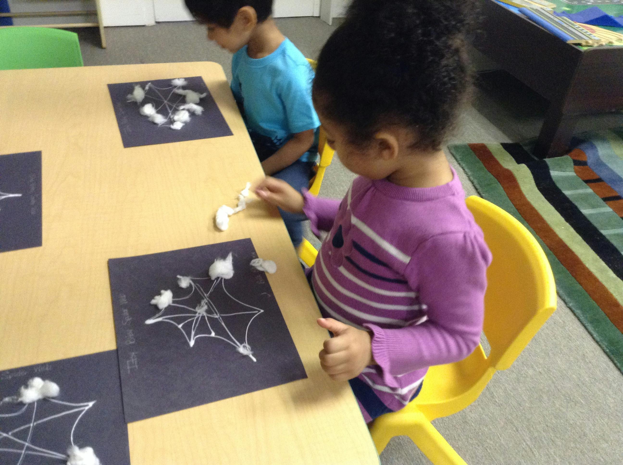 Children crafting paper spider webs with cotton balls at a table
