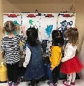 Four children painting on large white canvases