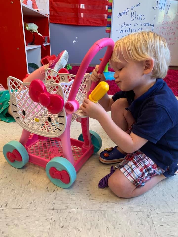 Child kneeling and playing with a pink toy shopping cart