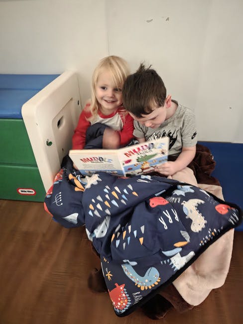 Two children reading a book together under a blanket