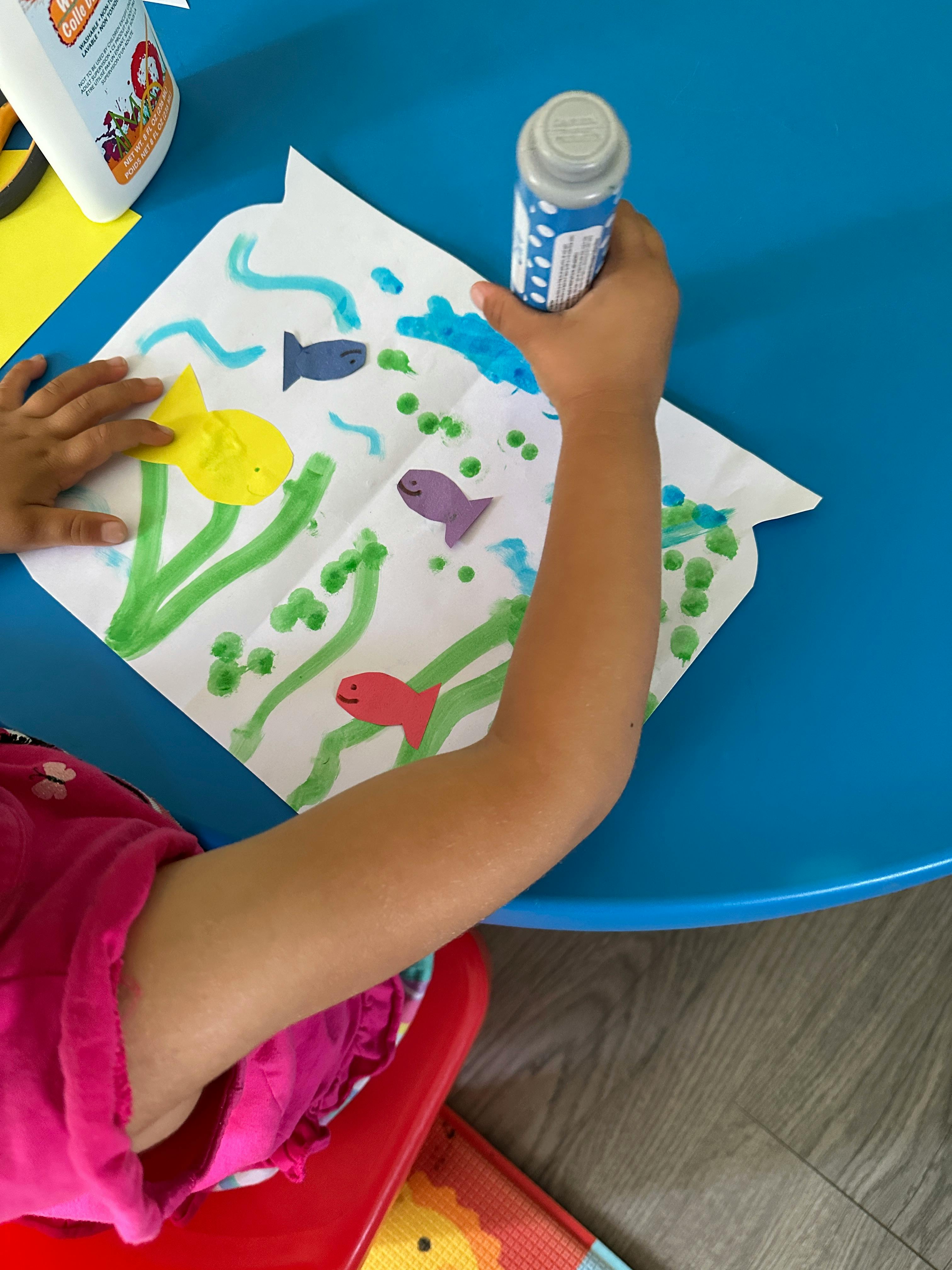 Child's hands working on a paper craft with fish cutouts and painted seaweed