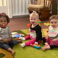 Three babies sitting on a rug with toys