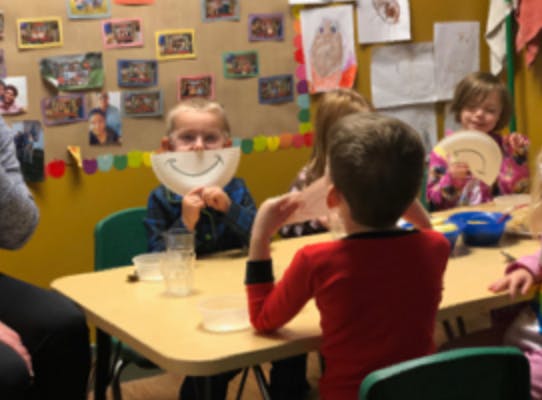 Child holding a paper plate with a smiley face in a classroom