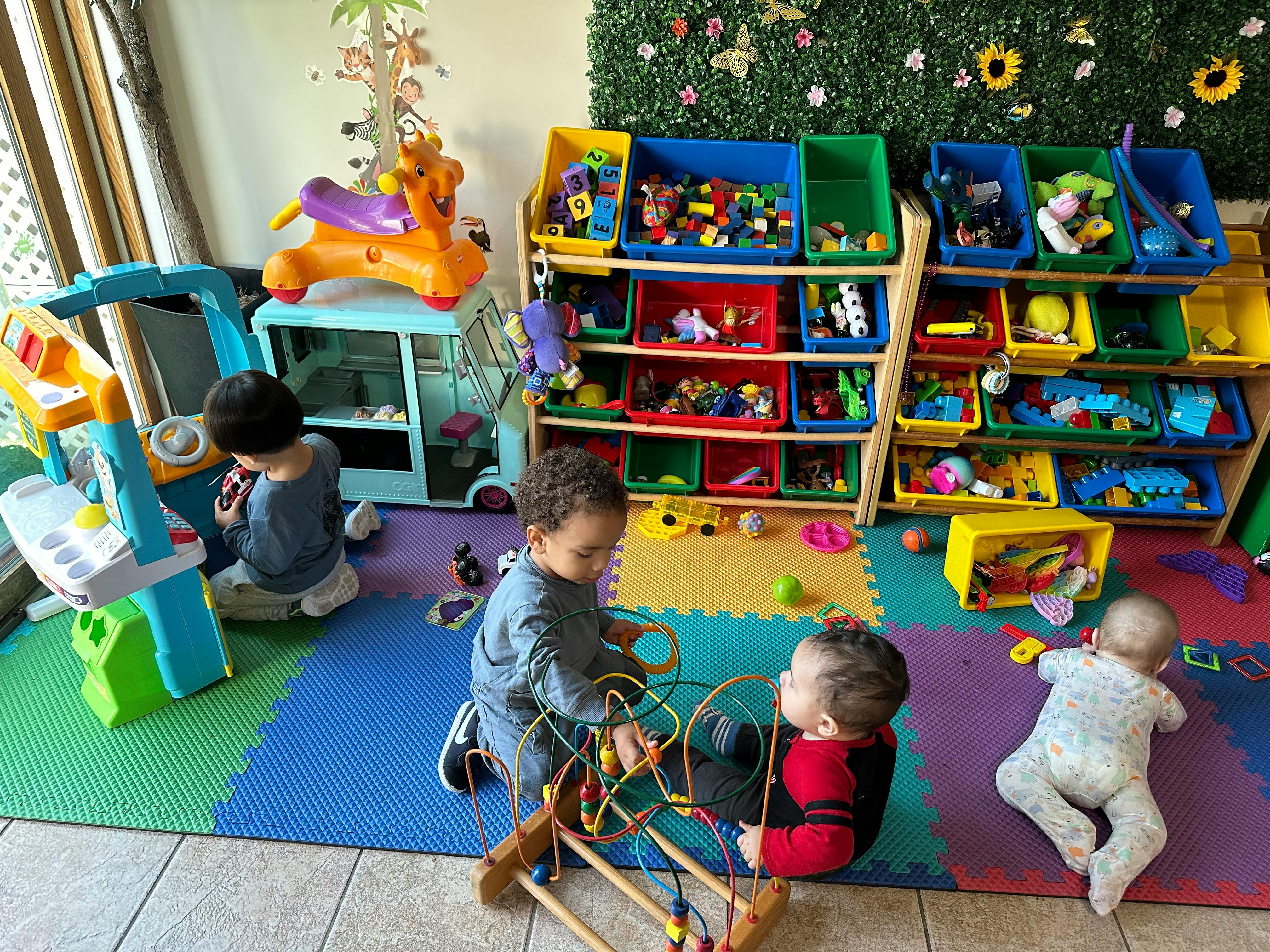 Three children playing with toys on a colorful mat in a playroom