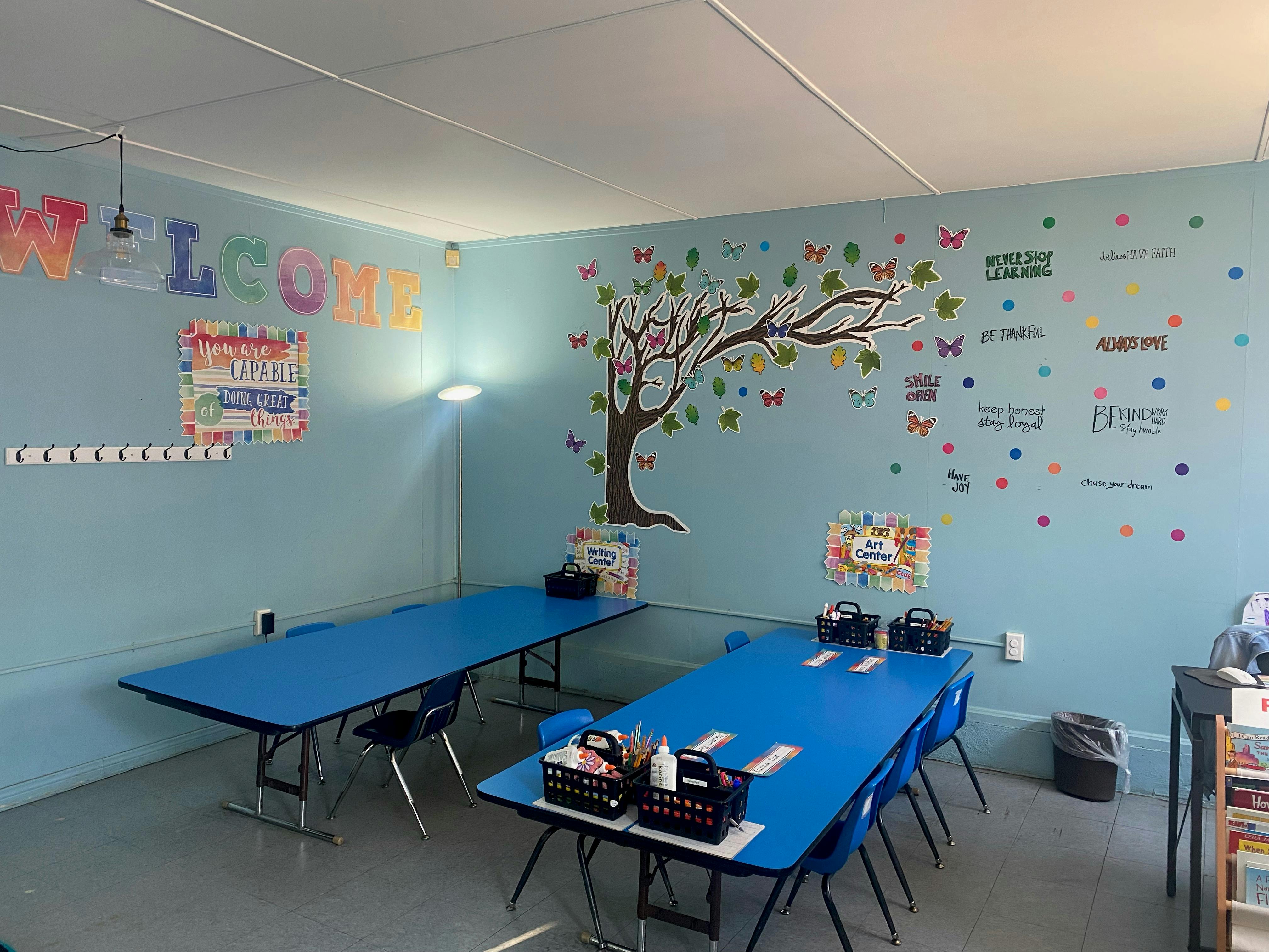 Classroom with blue tables and a tree mural on the wall