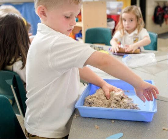 Child playing with kinetic sand in a blue tray