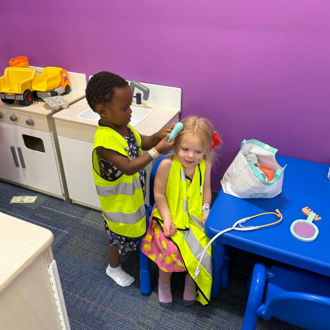 Two children in yellow vests playing, one brushing the other's hair