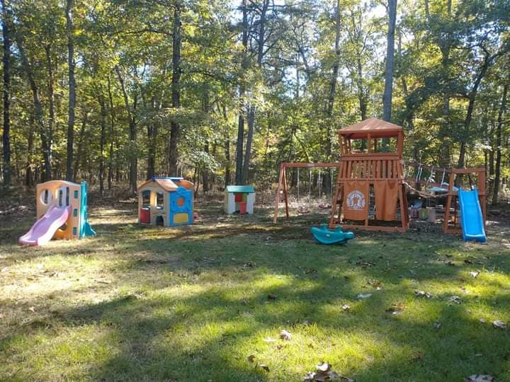 Playground with wooden playset, swings, and plastic playhouses in a wooded area
