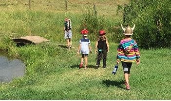 Four children walking in a grassy field next to a pond