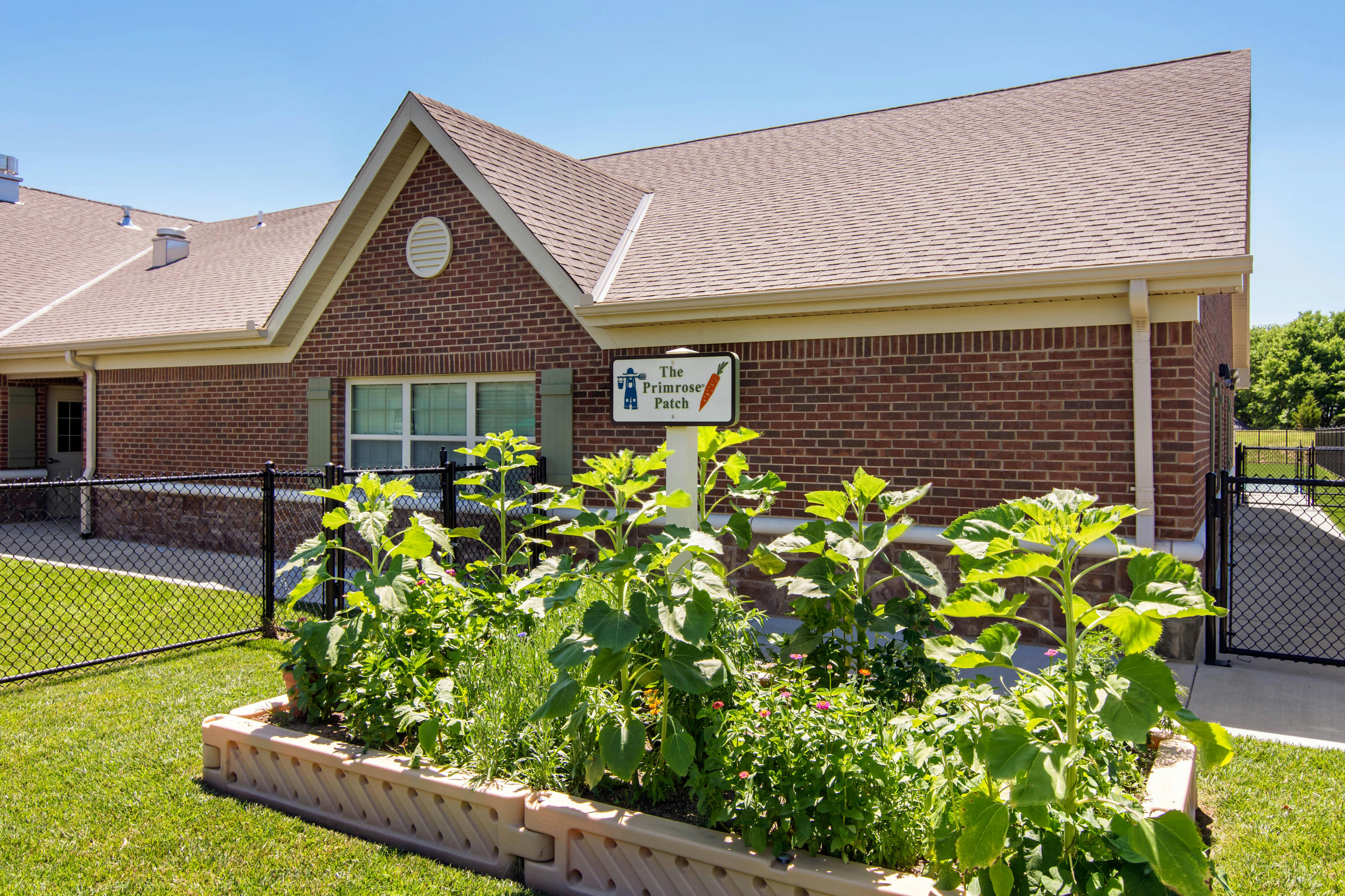 A brick building with a brown roof and a garden bed in the foreground
