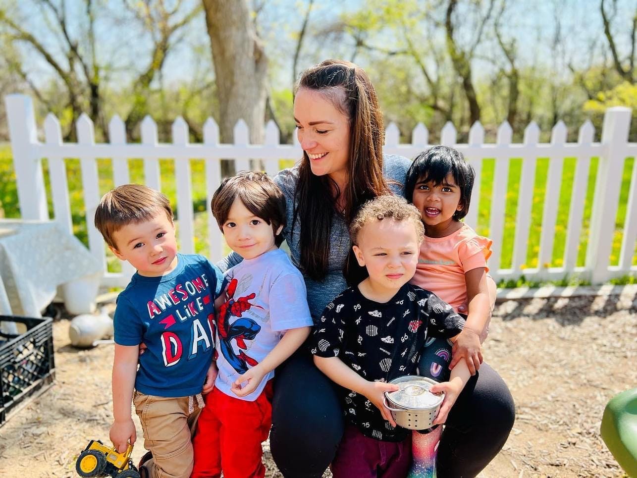 Adult and four children outdoors near a white fence