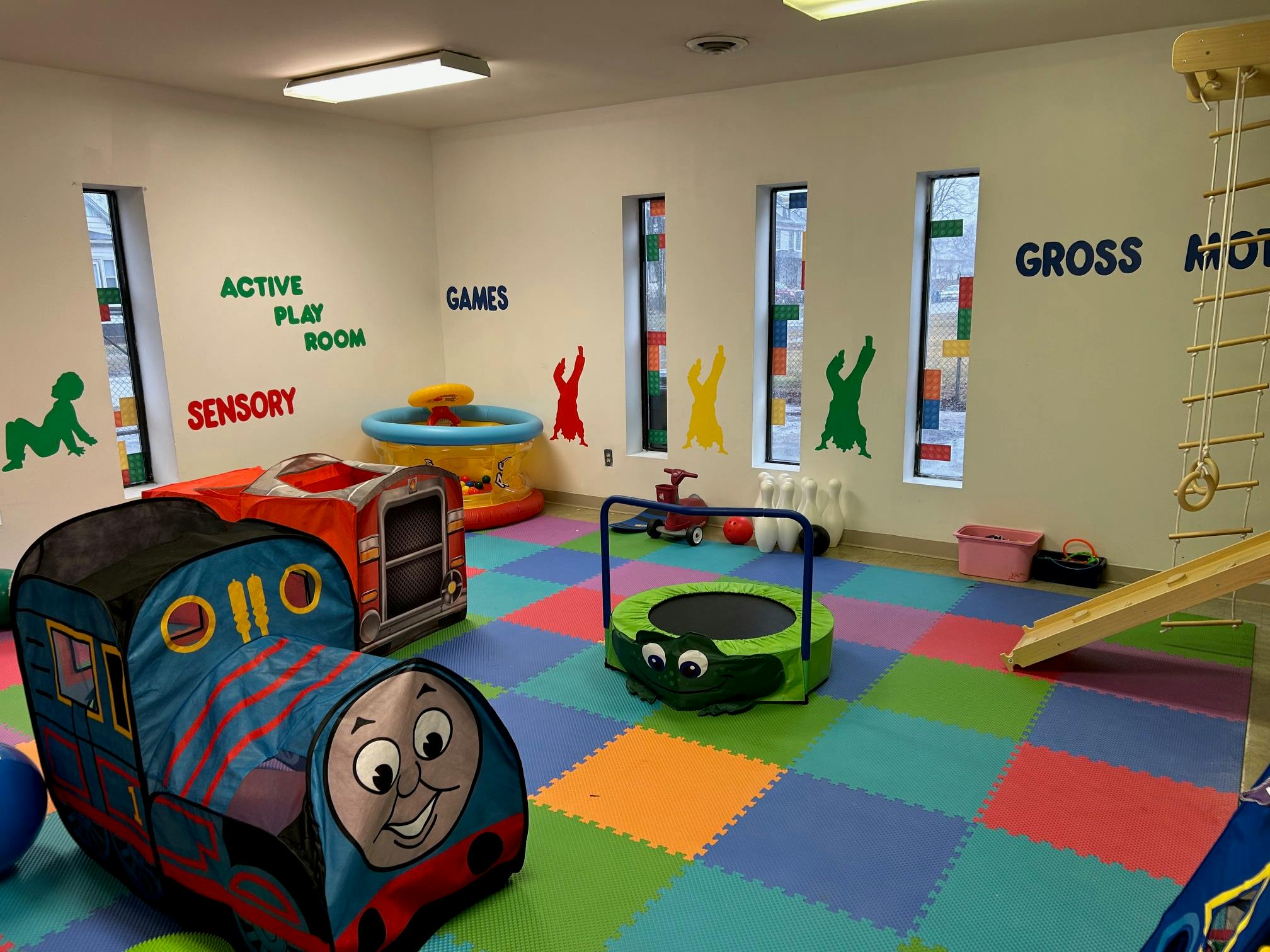 Indoor play area with a train tunnel, trampoline, and colorful floor tiles