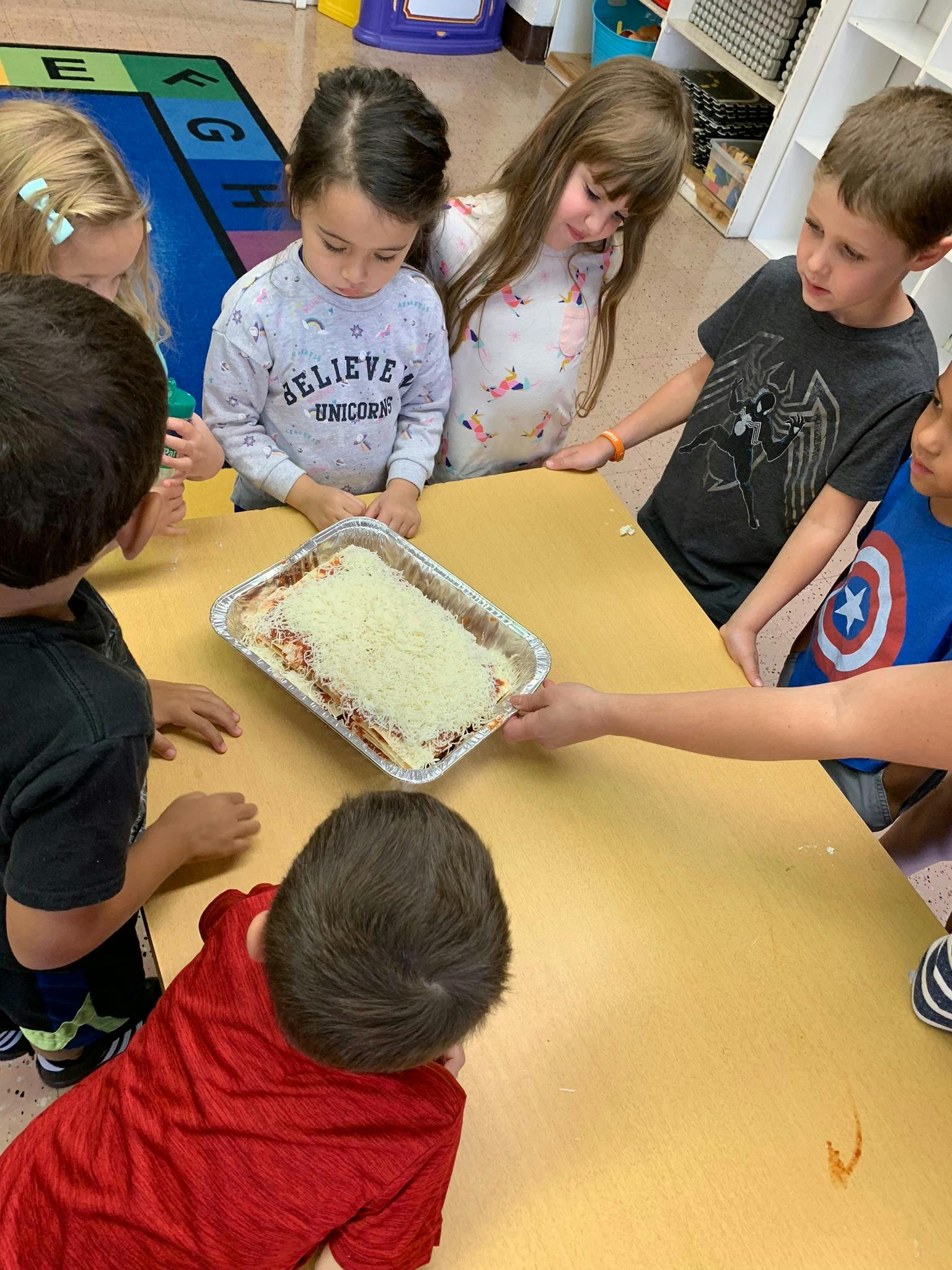 Children gathered around a table looking at a pan of food