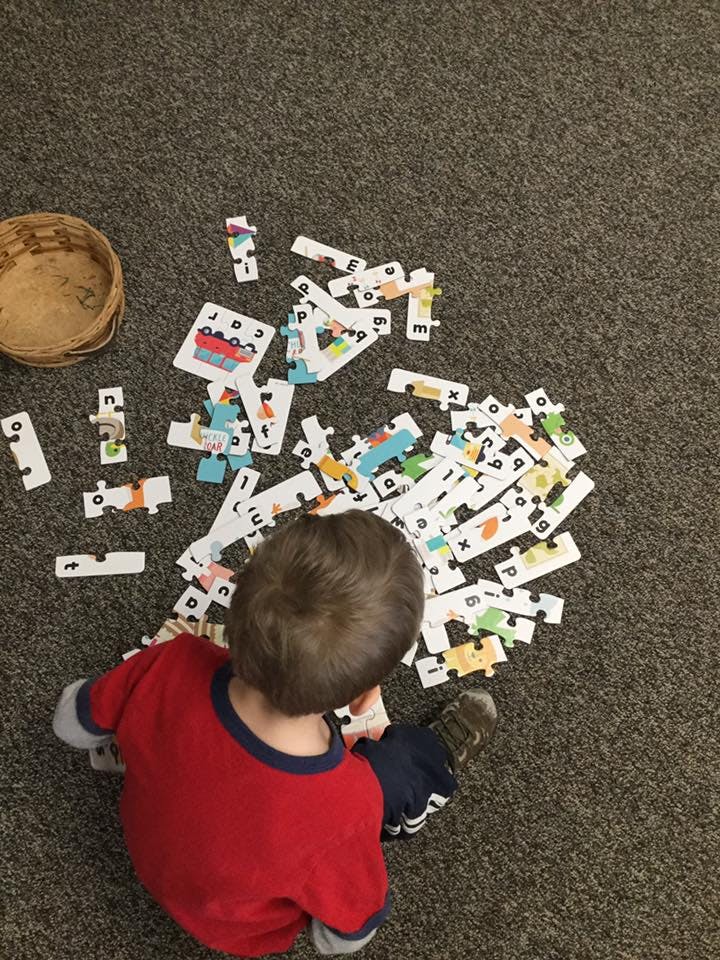 Child on floor playing with alphabet puzzle pieces