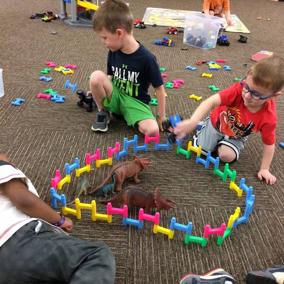 Children playing with colorful building blocks and toy dinosaurs on a carpeted floor