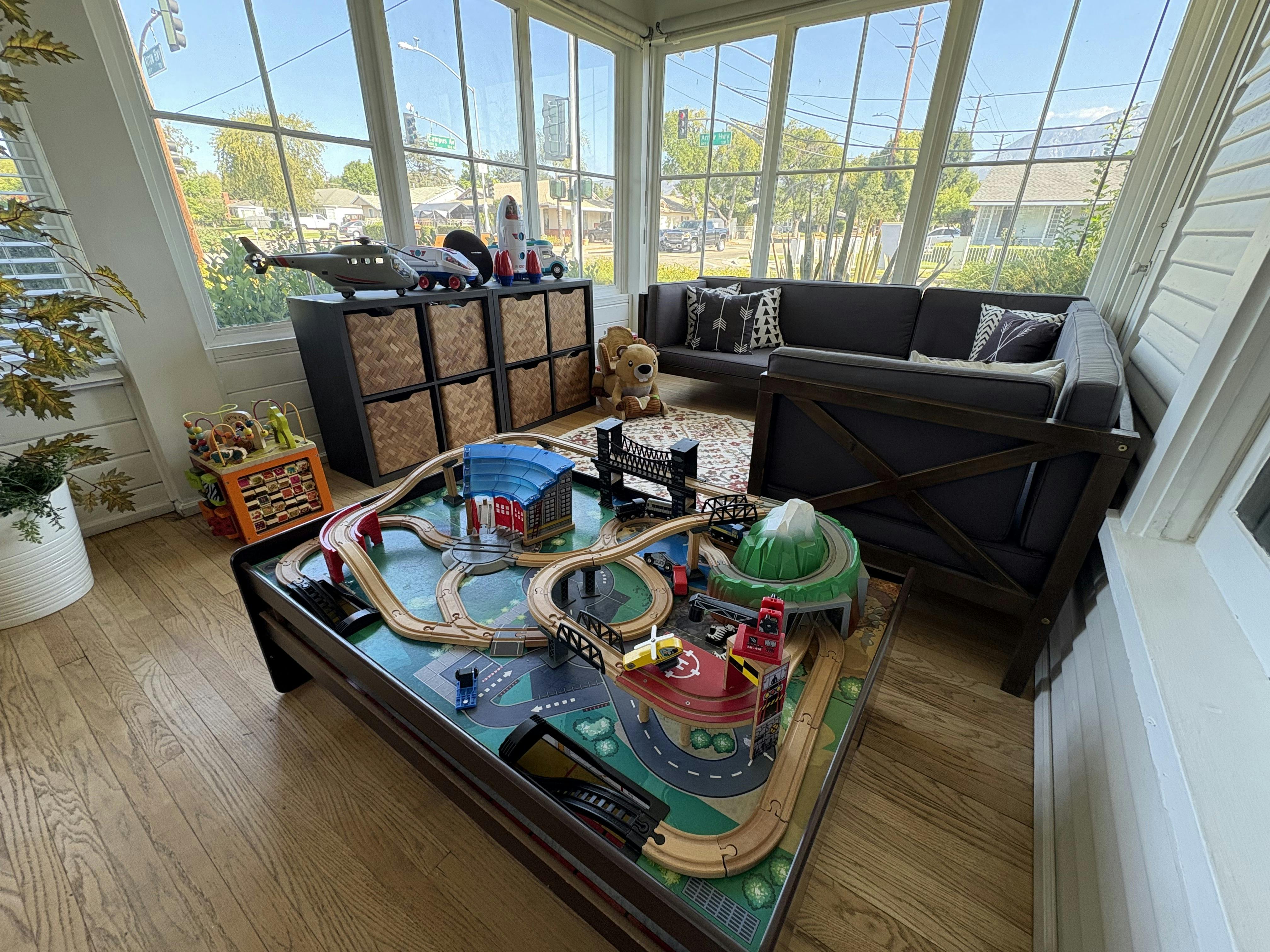 Wooden train set on a table in a sunroom with toys and seating