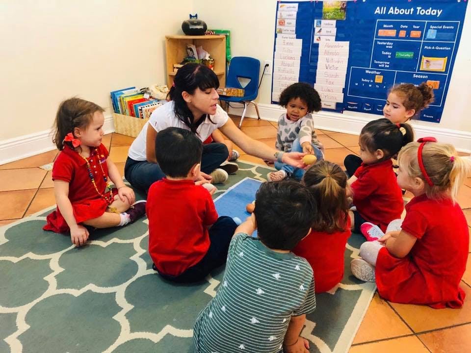 Adult person interacting with children sitting on a rug in a classroom