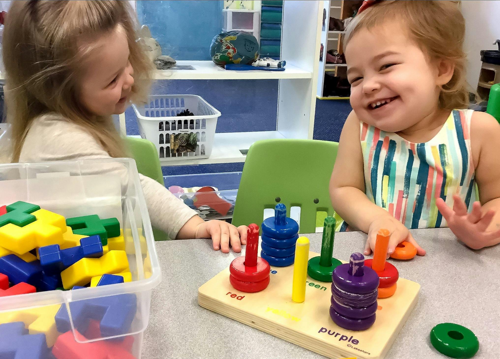 Two children playing with colorful stacking toys at a table
