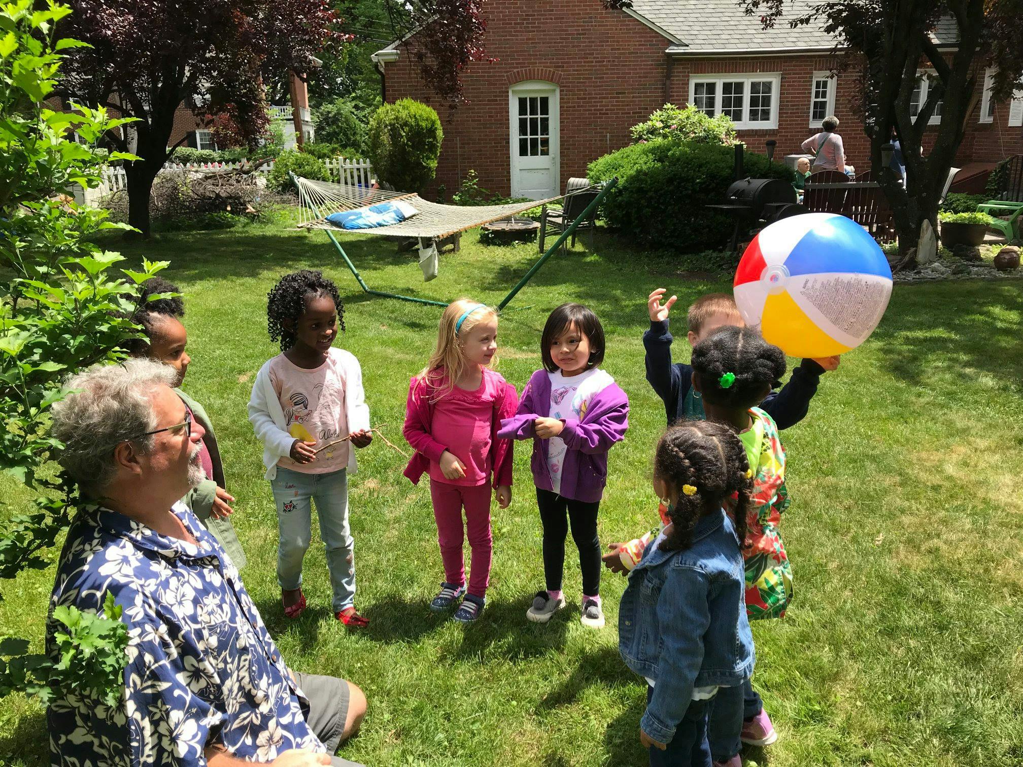 Person sitting on grass with children standing around, one holding a beach ball