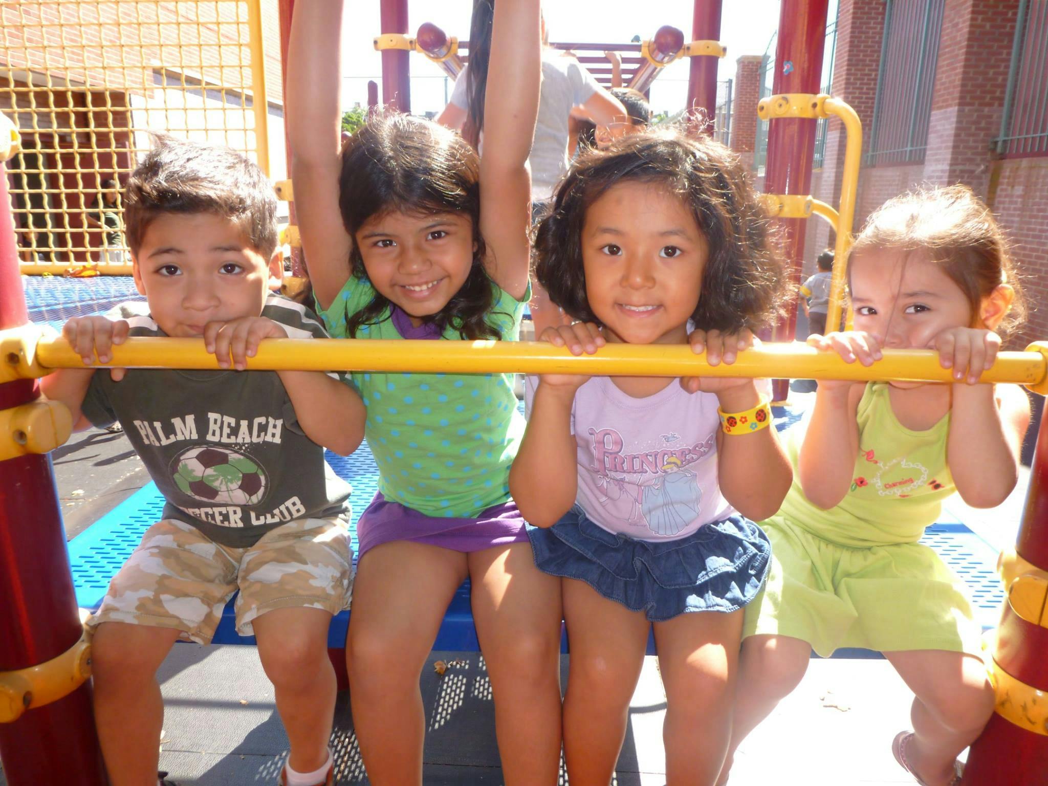 Four children sitting on a yellow bar on a playground