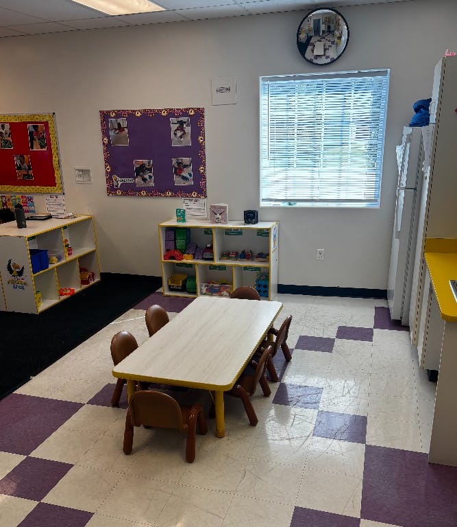 Classroom with small table and chairs, shelves with toys, and window