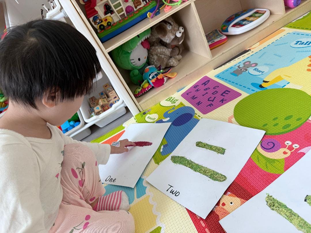Child drawing on paper with a red crayon